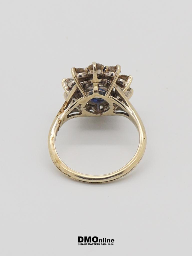 Gold engagement ring with a blue center stone and surrounding diamonds, viewed from the side.