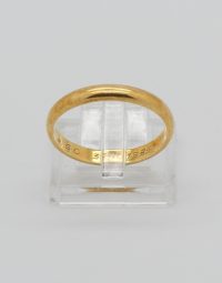 Gold wedding band displayed on a clear stand, with a subtle engraving along the inner edge.