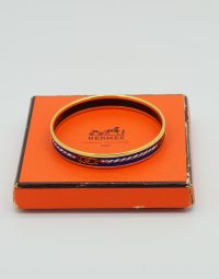 Orange Hermes box with a gold and blue enamel bangle resting atop it, the box showing wear on the edges.