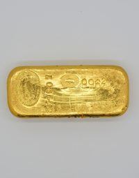 Gold bullion bar on a white background with stamped marks and round assay seal edge details visible on the surface.