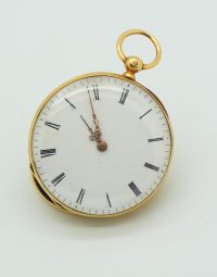 Antique gold pocket watch with Roman numeral dial lying on a light surface, ornate hands near 12 o'clock, with part of the case open.