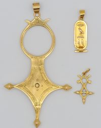 Gold pendant set with a large ornate cross-shaped frame featuring a circular bezel at the top and pointed ends, likely a decorative necklace piece.