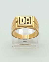 Gold signet ring with a square face showing the initials DA in black on a gold band, displayed on a clear stand.