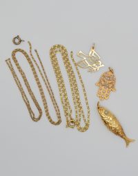 Assorted gold jewelry: two long chain necklaces, a small hoop earring, and fish, palm, and bird pendants on a light surface.