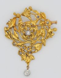 Ornate gold-tone floral brooch with leafy vines and pavé diamonds, featuring a dangling round diamond centerpiece at the bottom edge.