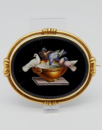 Round gold-framed artwork showing four pigeons perched on a golden bowl on a pedestal against a black background.