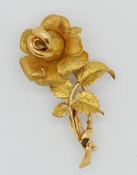 Gold-tone rose-shaped brooch with textured petals and curling leaves on a pale background