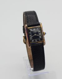 Vintage rectangular Cartier wristwatch with a black leather strap on a clear display stand.