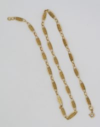 Gold chain necklace with ornate filigree oval links laid on a white surface.