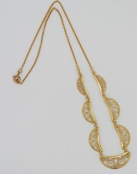 Gold necklace with decorative crescent filigree links connected along a chain and a curved pendant at the end.