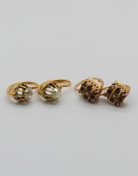 Two gold rings with clear gems and two square stud earrings with dark stones on a white background mix of jewelry pieces.