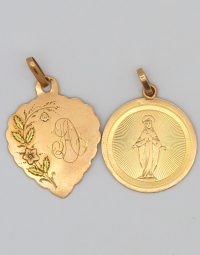 Two gold pendants on a light background: a heart-shaped charm with floral engraving and a decorative initial, and a round medallion depicting the Virgin Mary with radiating lines behind her.
