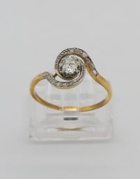 Gold ring with a central diamond and a curved, pave-set design on a clear display stand.
