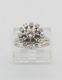 Silver halo diamond ring on a clear display stand, with a center stone surrounded by small pavé diamonds and a polished band.
